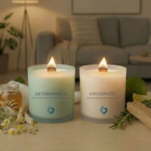 Aranżacja przytulnego salonu z zapalonymi świecami 'Łagodność' i 'Determinacja' na pierwszym planie. Ciepłe światło płomieni i miękkie tło z kanapą tworzą atmosferę relaksu i bezpieczeństwa. Wizualizacja wieczornego rytuału uziemienia i odzyskiwania spokoju w domowym zaciszu.